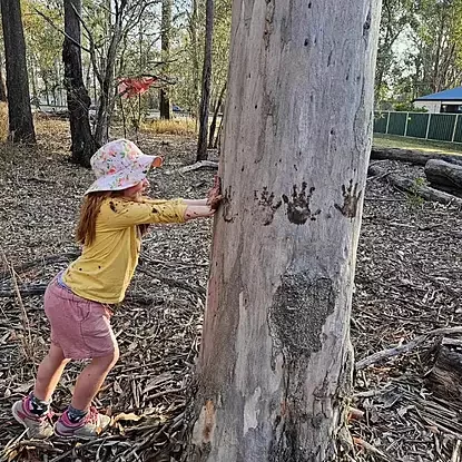 child playing with mud making handprints on a tree 